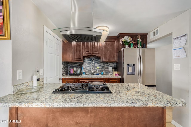 kitchen with light stone countertops, appliances with stainless steel finishes, tasteful backsplash, island range hood, and kitchen peninsula