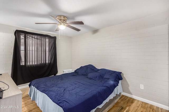 bedroom featuring ceiling fan, wood-type flooring, and brick wall