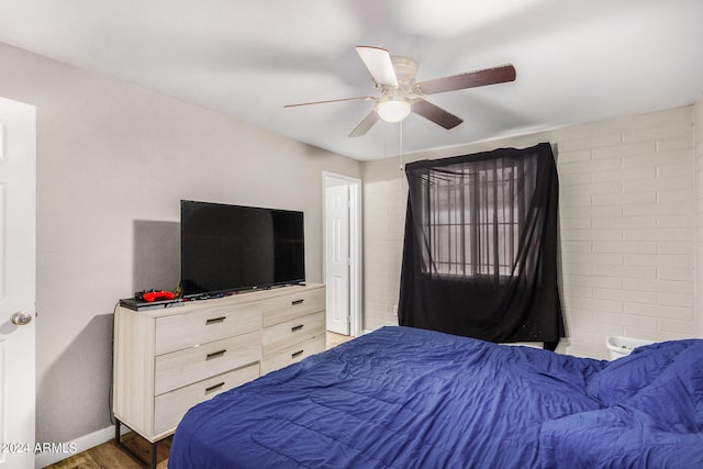 bedroom featuring ceiling fan, hardwood / wood-style flooring, and brick wall