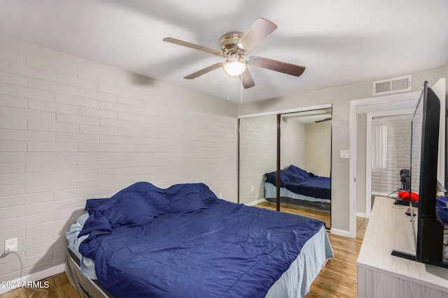 bedroom featuring brick wall, ceiling fan, a closet, and light hardwood / wood-style floors