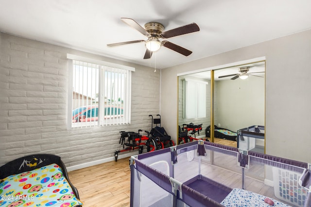 bedroom with a closet, ceiling fan, hardwood / wood-style flooring, and brick wall