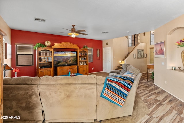 living room with stairs, visible vents, wood finished floors, and a ceiling fan