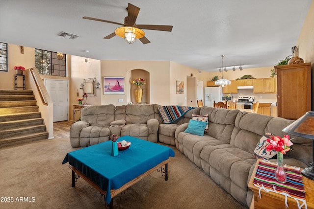 living room featuring stairs, light colored carpet, visible vents, and ceiling fan