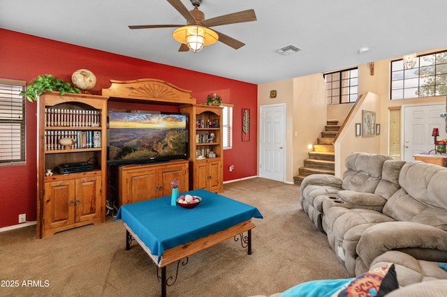 carpeted living room with visible vents, plenty of natural light, stairway, and a ceiling fan