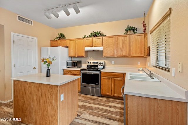 kitchen with light wood-style flooring, a sink, under cabinet range hood, appliances with stainless steel finishes, and light countertops