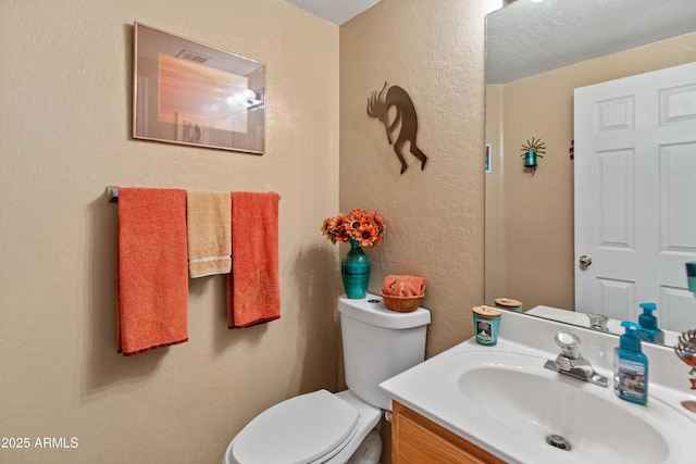 bathroom with vanity, toilet, and a textured wall