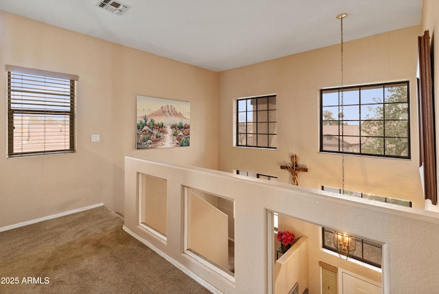 hall with a notable chandelier, baseboards, visible vents, and carpet floors