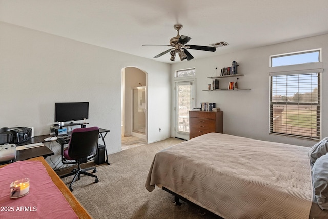 carpeted bedroom with arched walkways, visible vents, connected bathroom, and ceiling fan