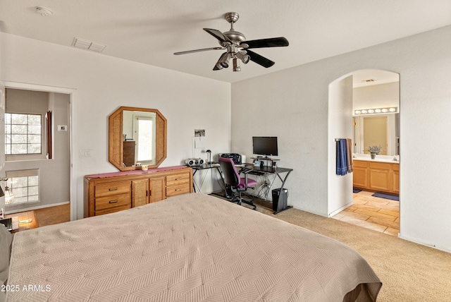 bedroom with visible vents, ensuite bath, arched walkways, ceiling fan, and light colored carpet