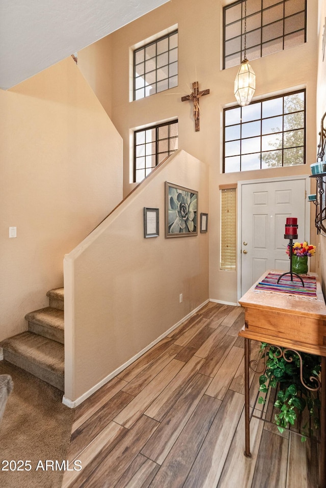 entryway with stairs, wood finished floors, a healthy amount of sunlight, and a towering ceiling