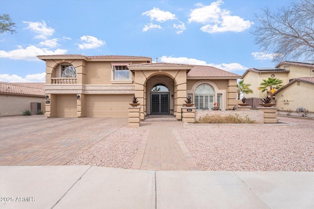 mediterranean / spanish-style home with a garage, decorative driveway, a tile roof, and stucco siding