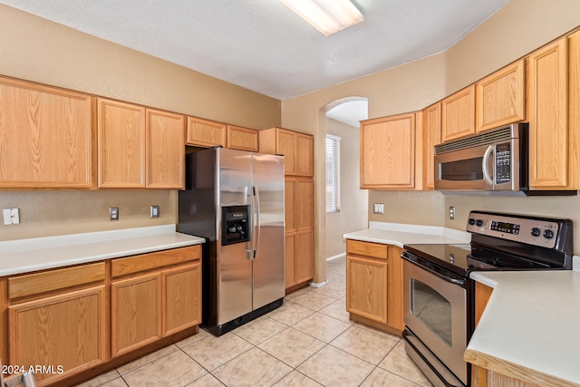 kitchen featuring light tile patterned floors, a textured ceiling, light brown cabinetry, and stainless steel appliances