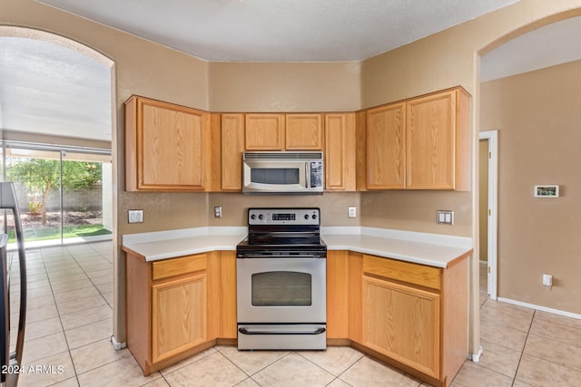 kitchen featuring light tile patterned floors, a textured ceiling, light brown cabinetry, and stainless steel appliances