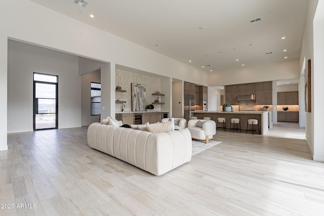 living room with a towering ceiling, wine cooler, and light hardwood / wood-style floors