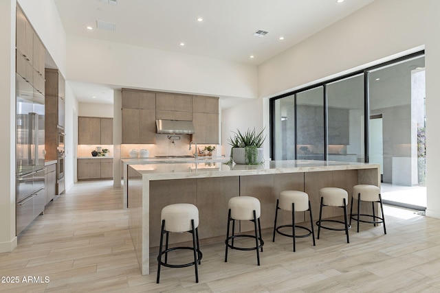 kitchen with light stone countertops, built in fridge, a large island with sink, and a breakfast bar area