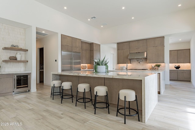 kitchen with a towering ceiling, wine cooler, backsplash, stainless steel built in refrigerator, and a breakfast bar area