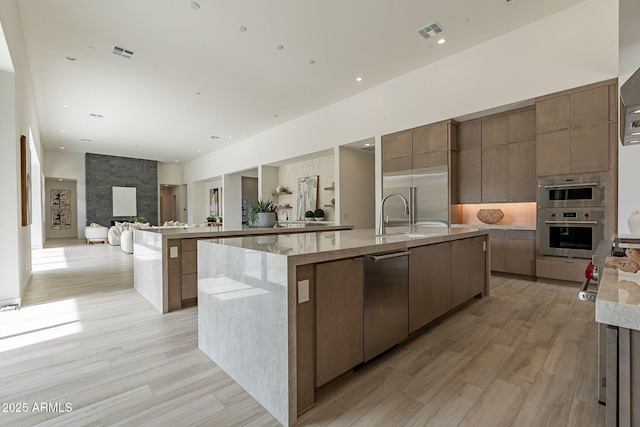 kitchen featuring stainless steel appliances, light hardwood / wood-style floors, a large fireplace, sink, and a large island with sink