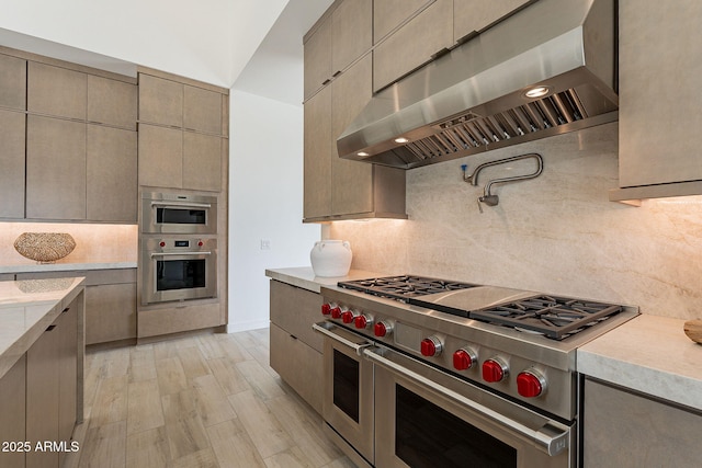 kitchen with decorative backsplash, light hardwood / wood-style floors, stainless steel appliances, and wall chimney exhaust hood