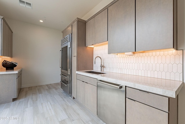 kitchen featuring gray cabinetry, light hardwood / wood-style floors, sink, stainless steel dishwasher, and tasteful backsplash