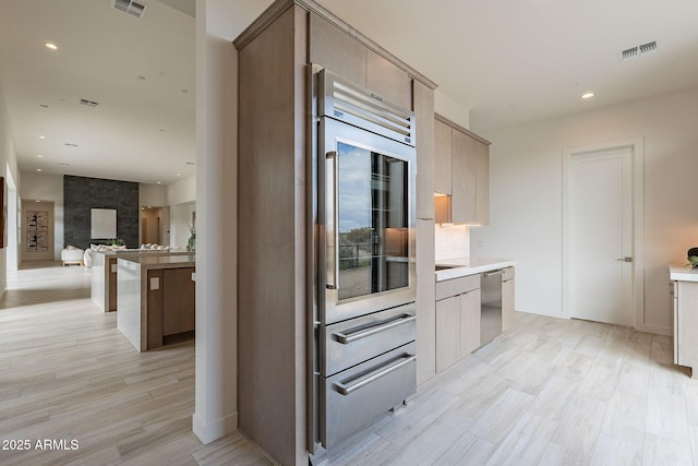 kitchen featuring light wood-type flooring, a kitchen breakfast bar, stainless steel dishwasher, light brown cabinets, and tasteful backsplash