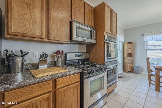 kitchen with dark stone countertops, ornamental molding, light tile patterned flooring, and appliances with stainless steel finishes