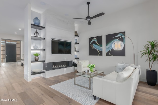 living room with built in features, a large fireplace, light wood-type flooring, and ceiling fan