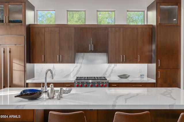 kitchen with a breakfast bar area, stainless steel range, light stone counters, and tasteful backsplash