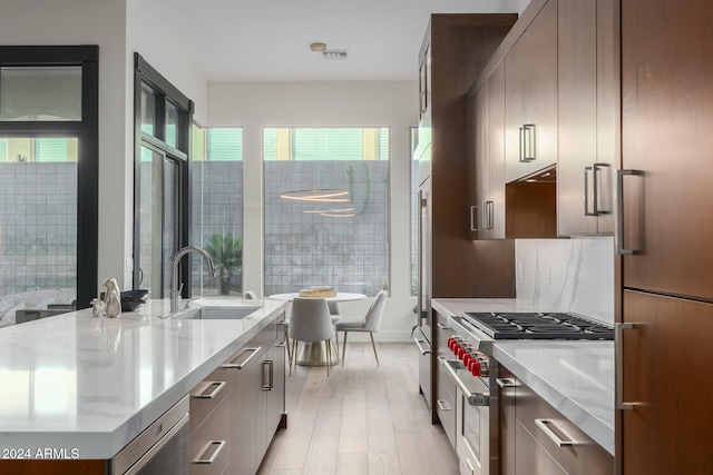 kitchen featuring fridge, stainless steel stove, sink, light stone countertops, and light wood-type flooring