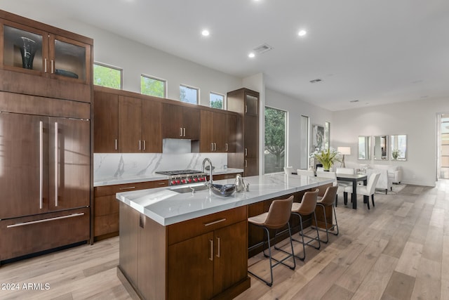 kitchen with sink, an island with sink, paneled refrigerator, and light hardwood / wood-style flooring