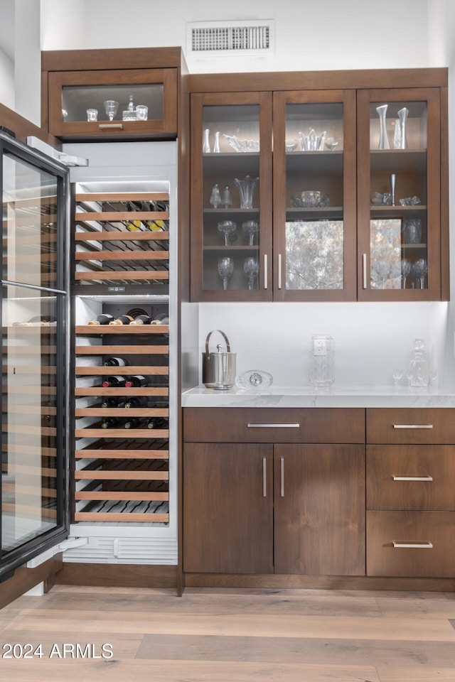 bar featuring wine cooler, dark brown cabinetry, and light hardwood / wood-style flooring