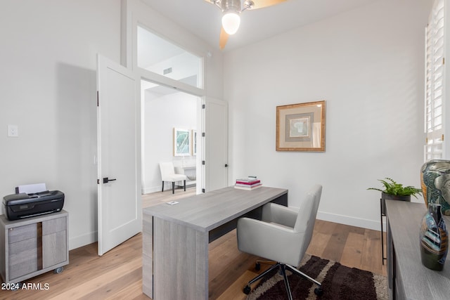 home office with a towering ceiling, light hardwood / wood-style flooring, and ceiling fan