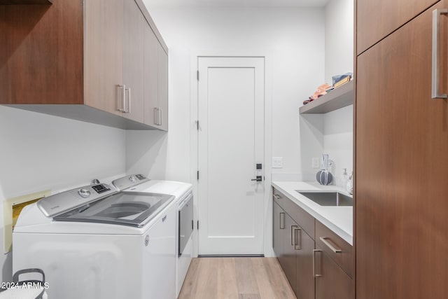 clothes washing area featuring washing machine and dryer, cabinets, light hardwood / wood-style flooring, and sink