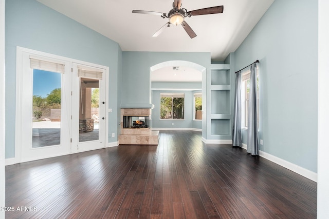 12120 E Cortez Dr, Scottsdale, AZ 85259 - unfurnished living room with arched walkways, ceiling fan, dark wood-style floors, built in features, and a multi sided fireplace