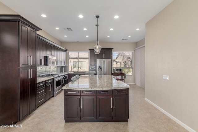 kitchen with a kitchen island, appliances with stainless steel finishes, decorative light fixtures, backsplash, and dark brown cabinetry