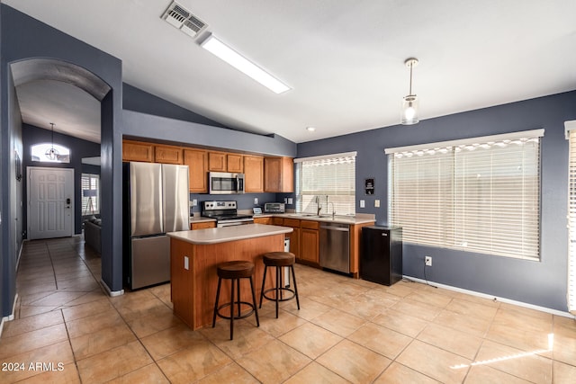 kitchen with appliances with stainless steel finishes, vaulted ceiling, a kitchen island, and hanging light fixtures