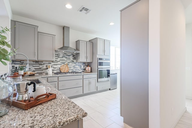 kitchen with appliances with stainless steel finishes, tasteful backsplash, sink, light stone countertops, and wall chimney exhaust hood