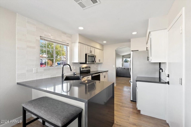 kitchen with kitchen peninsula, hardwood / wood-style floors, sink, white cabinetry, and appliances with stainless steel finishes