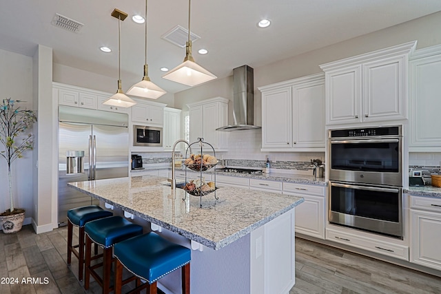 kitchen featuring wall chimney exhaust hood, tasteful backsplash, built in appliances, a kitchen island with sink, and white cabinets