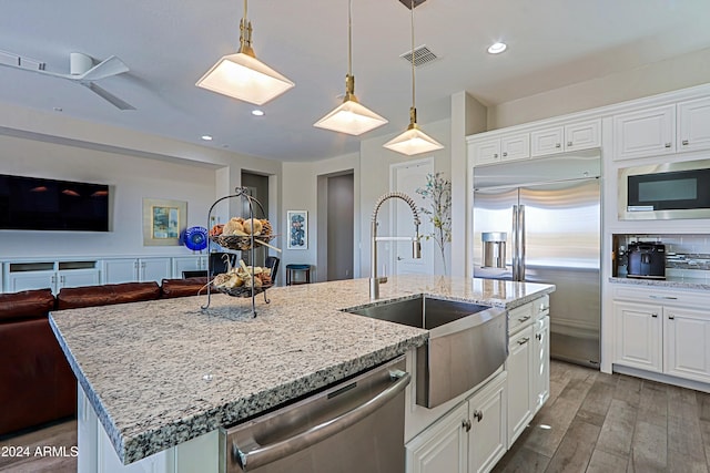 kitchen featuring built in appliances, white cabinets, an island with sink, and light hardwood / wood-style floors