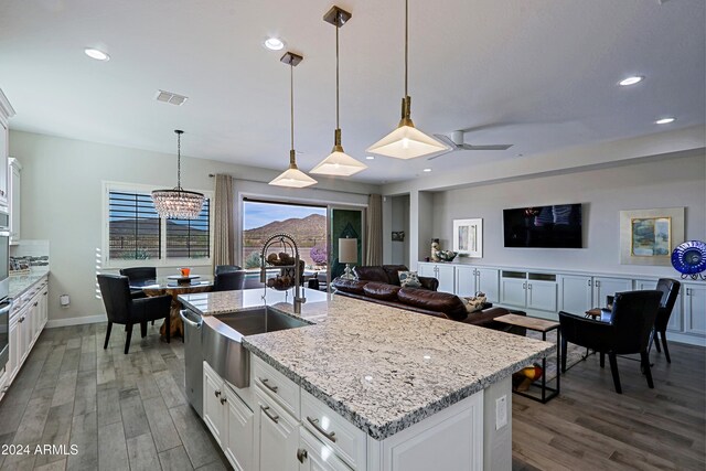 kitchen with ceiling fan with notable chandelier, dark hardwood / wood-style flooring, white cabinetry, and an island with sink