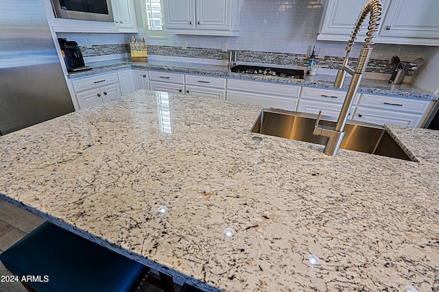 kitchen featuring light stone countertops, sink, tasteful backsplash, white cabinets, and appliances with stainless steel finishes