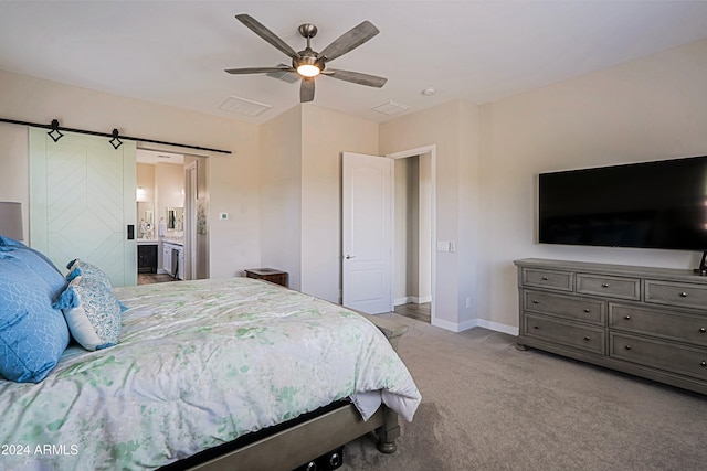 carpeted bedroom with a barn door, ceiling fan, and ensuite bath