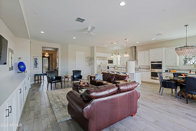 living room with ceiling fan with notable chandelier, light hardwood / wood-style flooring, and sink