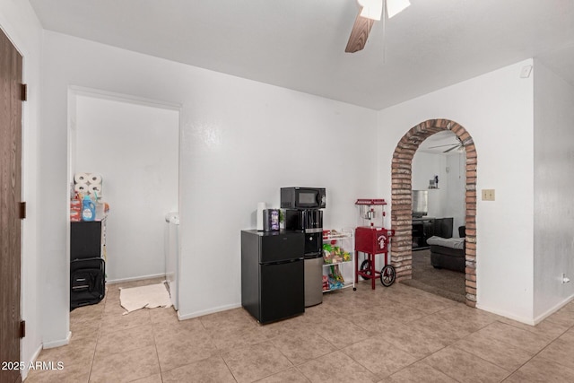 interior space with arched walkways, light tile patterned flooring, a ceiling fan, and baseboards