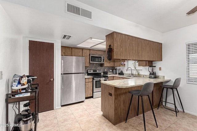 kitchen with stainless steel appliances, a peninsula, a sink, and visible vents