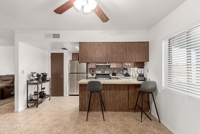 kitchen featuring stainless steel appliances, a peninsula, a sink, light countertops, and tasteful backsplash