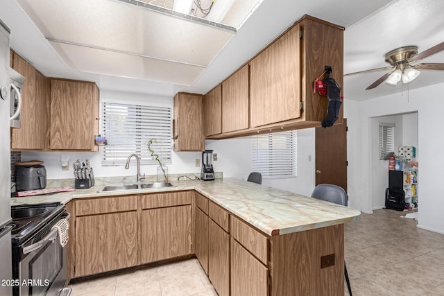 kitchen with light tile patterned floors, a peninsula, light countertops, stainless steel range with electric cooktop, and a sink