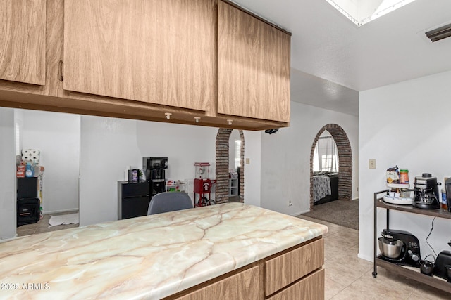 kitchen with arched walkways, light tile patterned flooring, a skylight, visible vents, and light countertops