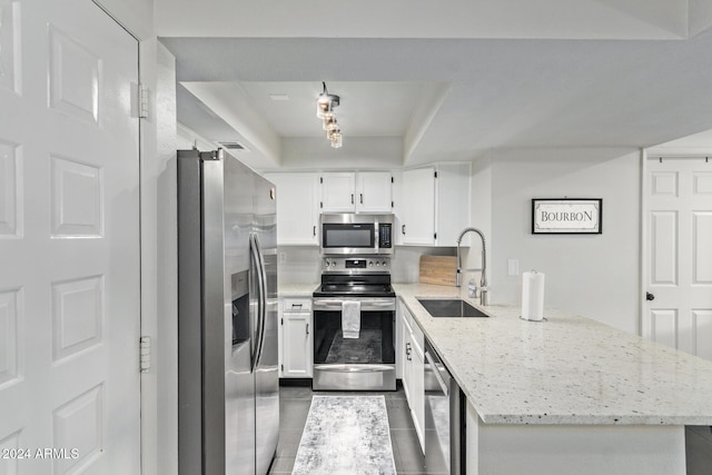 kitchen with light stone countertops, stainless steel appliances, sink, dark tile patterned flooring, and white cabinetry