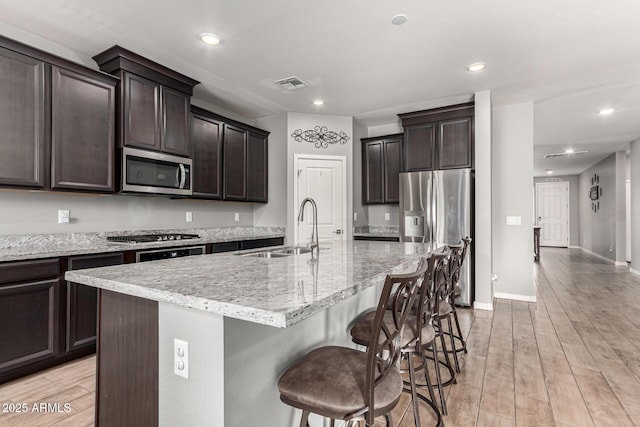 kitchen with stainless steel appliances, a sink, light wood-style flooring, dark brown cabinetry, and recessed lighting